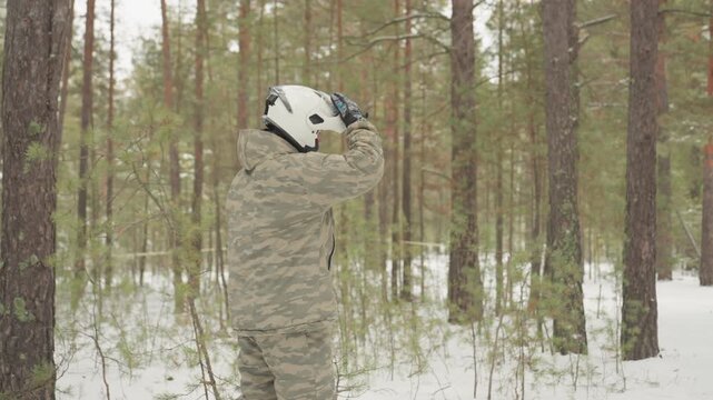 Atv rider inspects red quad in snowy pine forest, helmeted outdoors guide checks engine and gear before extreme offroad ride crisp cold air, tire tracks in snow, camo jacket, gloves, rear rack
