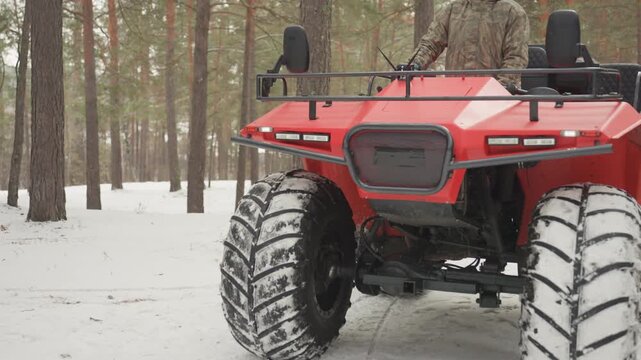 Red atv in snowy pine forest extreme offroad ride with rider maneuvering through packed snow, lowangle closeup of front wheels and sturdy grille, heavy tread tires kicking snow, rugged suspension