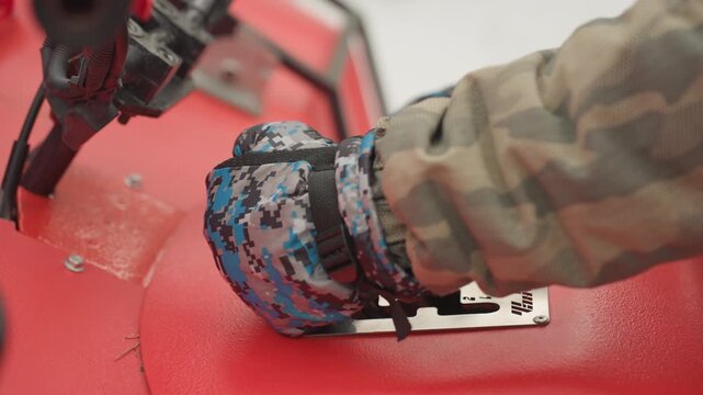 Gloved hand adjusts atv quad gear lever during preride check, camo jacket sleeve, blue patterned gloves, firm grip on shift gate, readiness for rough terrain, highenergy adventure tone