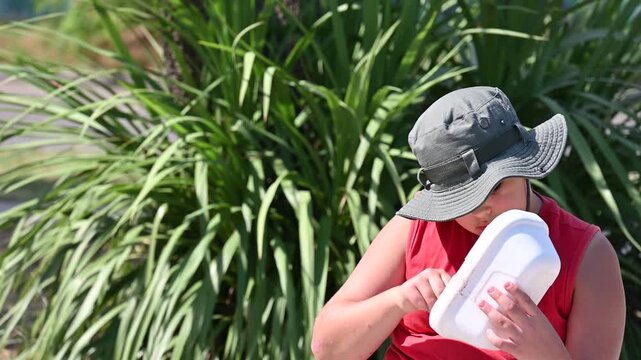 person sitting and eating from plastic container in summer park