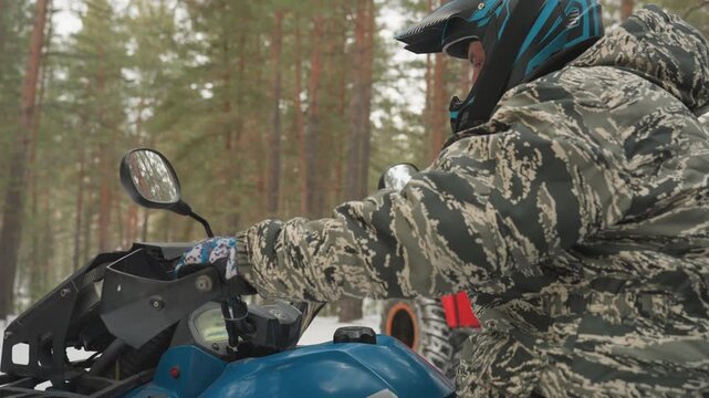 Snowy pine forest rider on atv controls, camo suit and helmet, gloved hands on throttle and handlebar, blue quad idling among trees, quiet winter atmosphere, frost on tire and mirror, focused steady