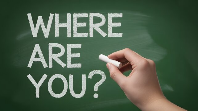 A human hand writes the question WHERE ARE YOU in white chalk on a dark green chalkboard surface for seeking a