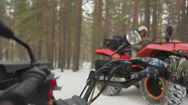 Closeup atv handlebars in snow, red quad parked among pine trees, gloved hand on throttle, mirror reflecting distant rider, winter cold, prepping for extreme offroad ride, guide inspects controls,