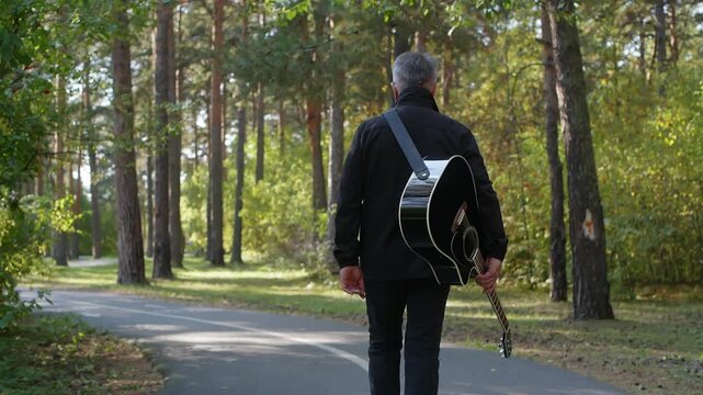 Solo man with guitar walks down shaded forest path, tall pines and dappled sunlight, steady stride, shoulder strap swing, introspective mood, ambient nature rhythm, cinematic single take
