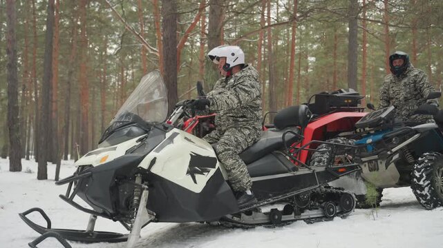 Three riders on snowmobiles and atvs gather in snowy pine forest, camo jackets and helmets, engines idling, close inspection of treads and gear, teamwork and route planning before offroad expedition,