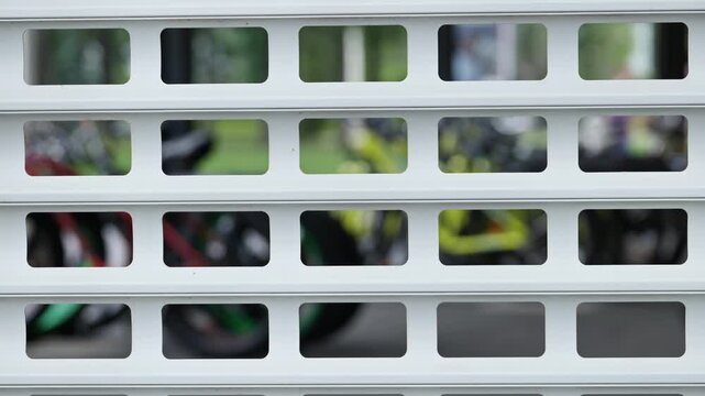 White geometric metal security shutter with a blurred, colorful background of bicycles in a park