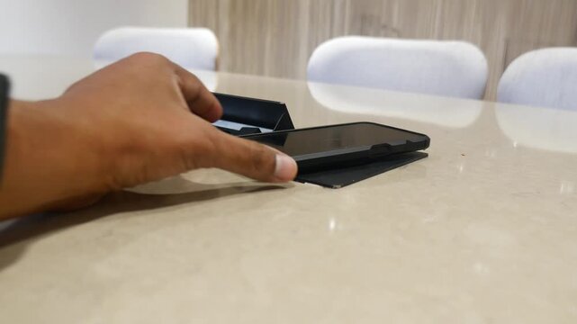 A person placing mobile phone on an in-built wireless charger on meeting table in modern office, showcasing convenient technology at work.