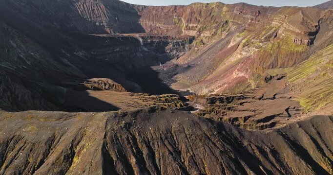 Vanuatu, Ambrym Island volcano caldera showcasing Benbow and Marum craters, with dark volcanic rock formations, eroded slopes, and hints of green vegetation under cloudy sky. Aerial view drone flight