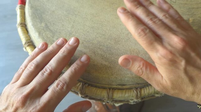 Top view of caucasian white hands playing a rhythmic beat on an african djembe drum