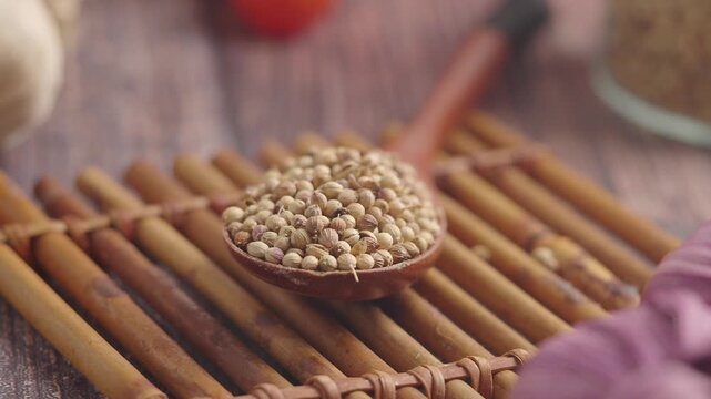 Coriander seeds on wooden spoon over bamboo mat macro footage showing traditional spice arrangement for cooking.