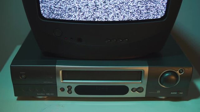 man hand pulls out a VHS cassette and inserts another movie tape into an old VCR sitting under a bulky CRT television. Nostalgic 90s home entertainment moment, warm analog atmosphere.