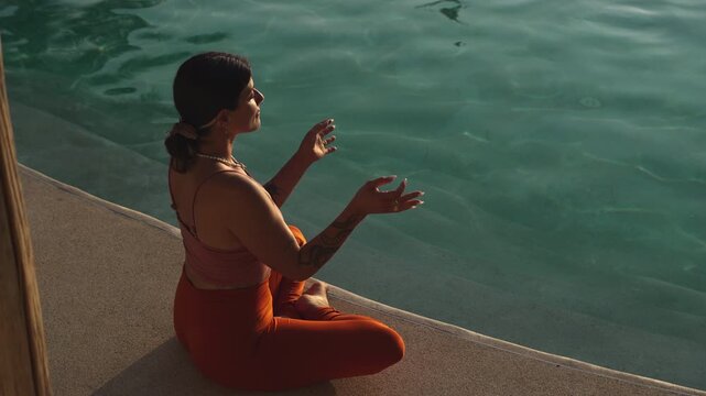 Young women sitting crossed legged by the pool during sunset in mediation 
