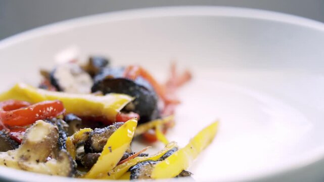 Chef adding colorful roasted vegetables to white plate using blue tongs, close-up