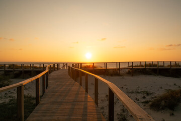 Fototapeta premium Wooden path at Costa Nova d'Aveiro, Portugal, over sand dunes with ocean view, evening. Wooden footbridge of Costa Nova beach . Aveiro, Portugal.