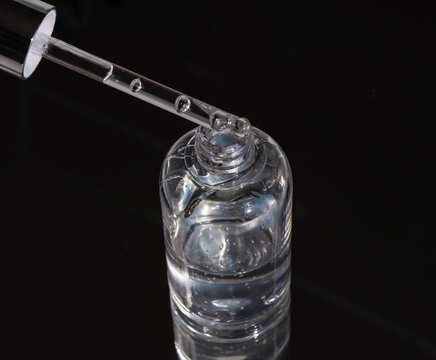 Suspended serum drop falling from silver dropper into transparent bottle on dark. Emphasizes clinical purity and concentrated active ingredients for premium skin treatment marketing.