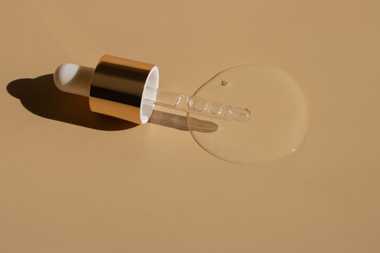 Clear serum texture spill with gold-capped dropper casting strict shadows on tan surface.