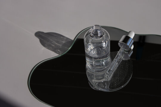 Glass cosmetic container on a wavy reflective mirror with harsh daylight shadows. Radiates organic purity and innovative aesthetics. Excellent for clean beauty branding and minimalist skincare promo.