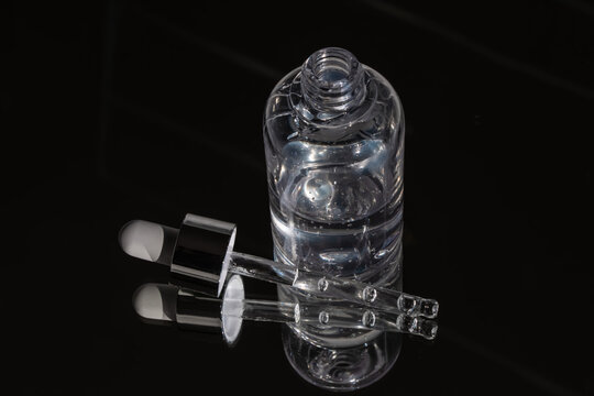 Clear cosmetic vial and silver pipette on reflective black glass. Symbolizes pure hydration and advanced dermatological science. Ideal for premium skincare beauty ads.