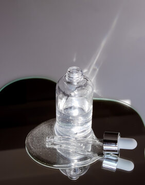 Close-up of transparent serum bottle on mirror reflecting light beams. Signifies clinical clarity and illuminating skin treatments. Fits high-end dermatological packaging presentations.