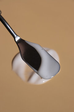 Stainless steel cosmetic spatula spreading rich white cream across a smooth beige surface. Optimal for premium moisturizer and lotion advertising.