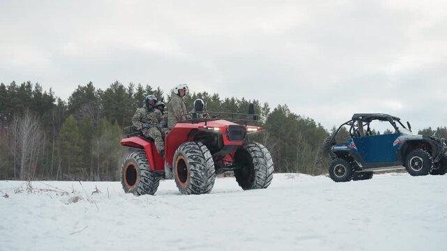 Red atv and blue utv in snowy field with caucasian riders preparing for extreme winter ride, pine forest backdrop, chunky snow tires, helmets and camouflage jackets, idle engines, crisp cold light,