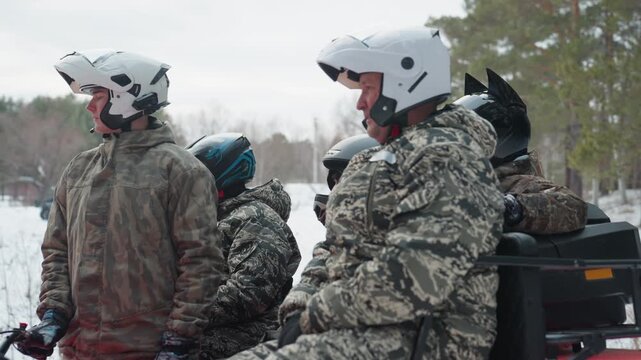 Winter atv ride through snowy forest, red quad carrying bundled riders in camouflage jackets and helmets guide and driver prepare at trailhead, engine rumble, tires kicking snow along pinelined path,