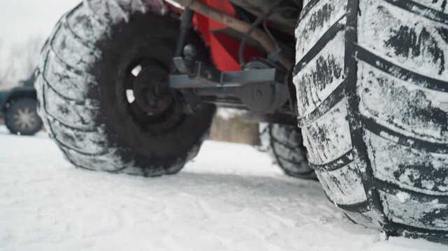 Snowcovered path with rugged vehicle. All terrain vehicle navigating icy snowy landscape quickly. Closeup of ATV tire gripping icy snow with mechanic testing traction in frosty wilderness