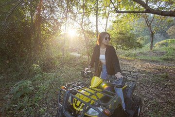 Confident young woman sitting on yellow atv in green forest enjoying beautiful golden sunlight during an outdoor nature adventure feeling relaxed and happy on quad bike offroad trail © CoreRock