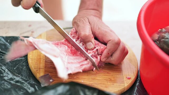 Close up of hands using knife to cut raw fish on wooden board, preparing food.