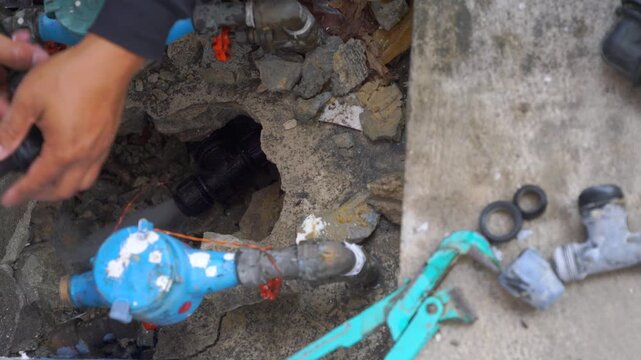 Technician hands repairing underground water pipe and meter system in concrete hole. Maintenance worker fixing leak with tools and fittings. Public utilities infrastructure service worksite.