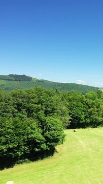 Scenic view of green fields, hay bales, and forested hills under a clear blue sky in the Morvan countryside, France.