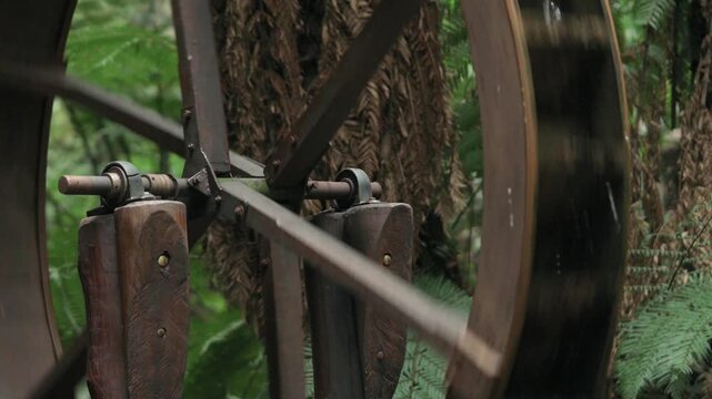 Detailed close up shot focusing on the wooden spokes and rustic structure of a traditional water wheel in a green forest environment.