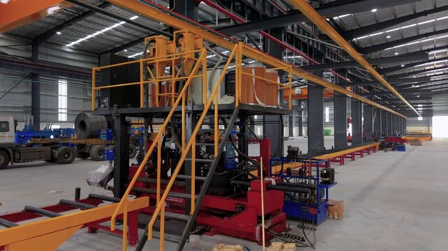 A wide interior shot of a modern industrial warehouse featuring heavy engineering production lines, automated machinery, and steel coil transport trucks.
