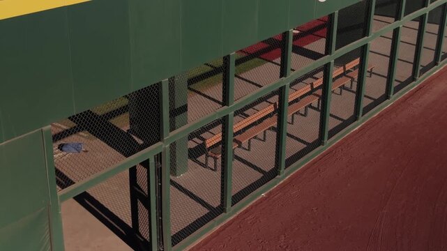 Slow steady pan along empty bullpen bench area with green fencing and red warning track