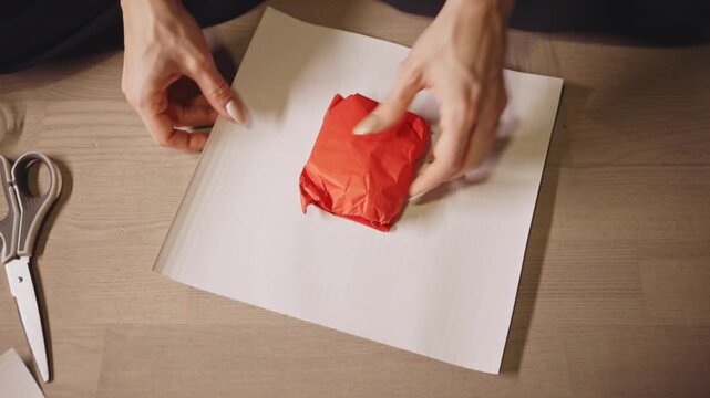 Hands Carefully Fold Striped Wrapping Paper Around a Small Christmas Gift - Close Up