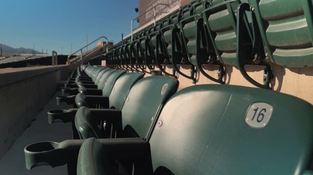Steady forward glide past empty stadium seats and cup holders under clear daytime light