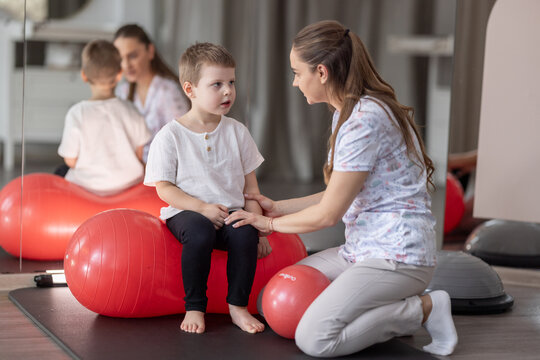 Pediatric Physical Therapist Working With Young Boy on Exercise Ball During Rehabilitation Session At Clinic