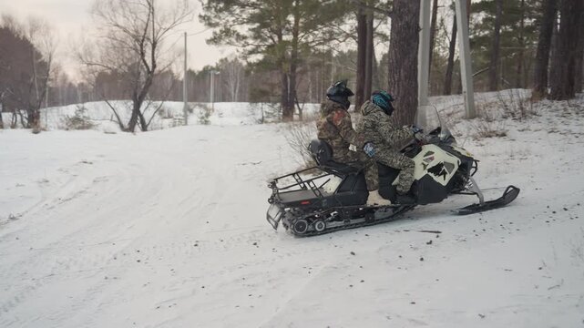 Two caucasian riders on snowmobile crossing snowy field, camouflaged jackets, cautious pace toward pine forest, overcast sky, cold breath, parallel tracks in powder, scouting maneuver