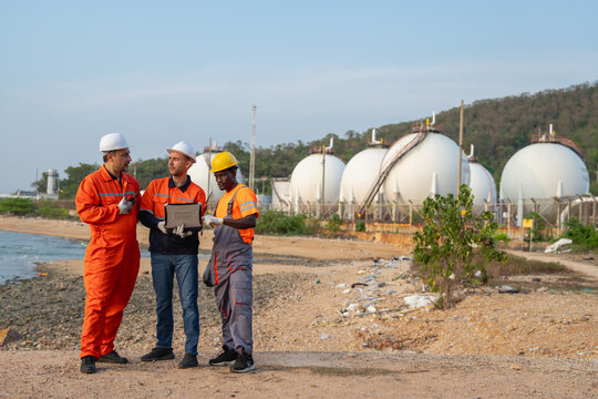 Three engineers collaborate on safety measures at industrial gas facility by the shoreline
