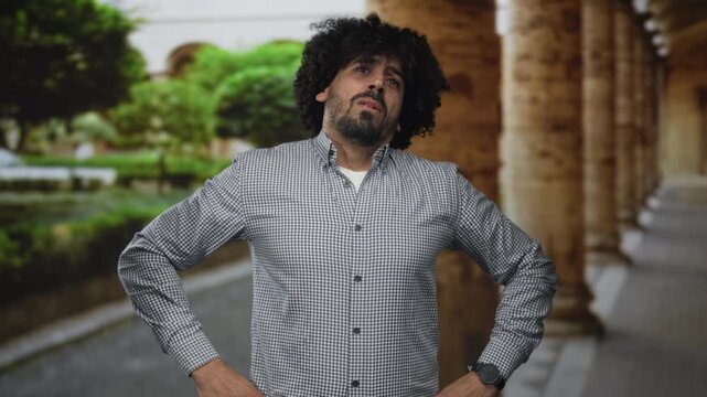 Man with curly hair gesturing with both hands toward a building colonnade, palms visible in a pleading gesture; frustration plea.