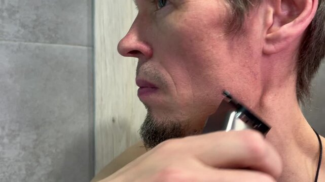 Man trims facial hair in bathroom using electric trimmer for neat look