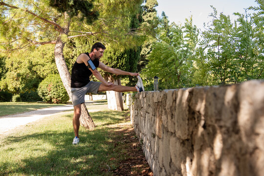 Man stretching leg outdoors by stone wall in park scene