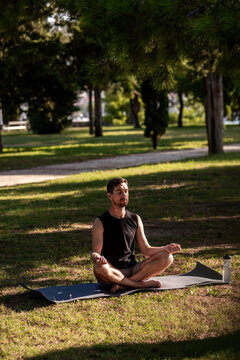 Man practicing yoga meditation on mat in sunny park