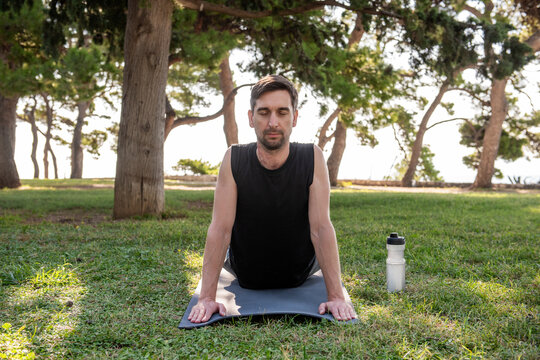Man practicing outdoor yoga pose on mat in park grass
