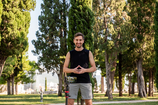 Male yoga instructor in park filming outdoor workout video