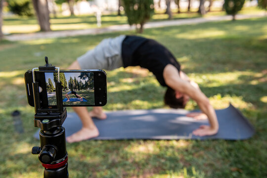 Man practicing yoga bridge pose in park with camera setup