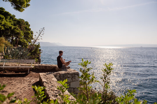 Man meditating in yoga pose on rocky ledge by the sea