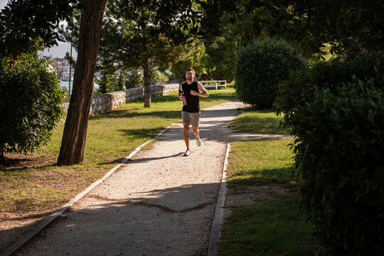 Man jogging on sunny park path surrounded by trees