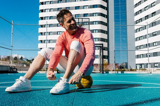 Man tying shoelace on street basketball court in city