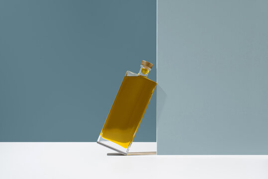 Minimal bottle of olive oil leaning on pastel wall background